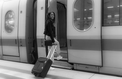 Full length portrait of young woman entering train with luggage at railroad station