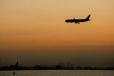 Silhouette airplane flying in sky during sunset