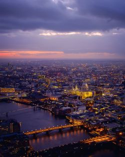 Aerial view of illuminated buildings and thames river against cloudy sky at dusk