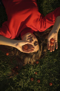 Young woman in red dress holding cherry tomatoes while lying on grass during sunny day