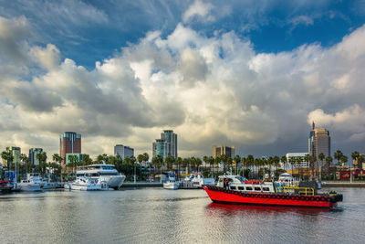 Boats in river by buildings in city against sky