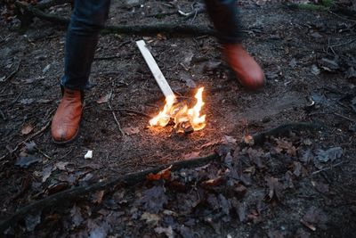 Low section of man standing by bonfire in forest