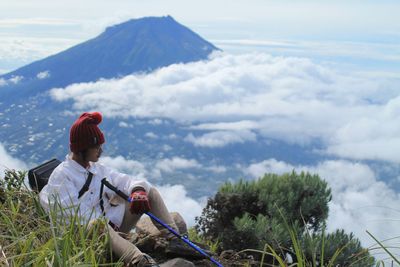 Man sitting on mountain against sky