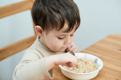 Little boy eating oatmeal for breakfast in the kitchen