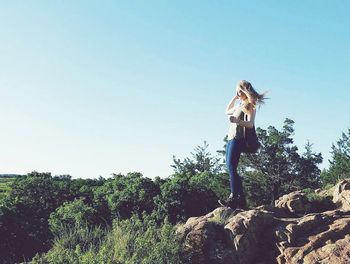 Full length of woman standing on rock by trees against clear sky