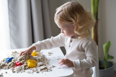 Cute happy kid playing with kinetic sand indoors.motor sensoric skills concept.