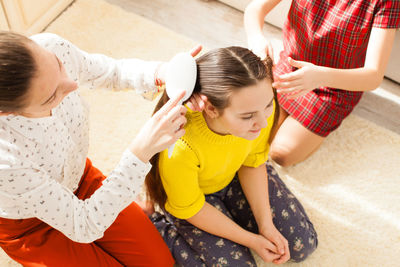 Mother combing hair of daughter at home