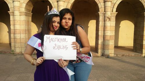 Portrait of smiling females showing placard while standing against building