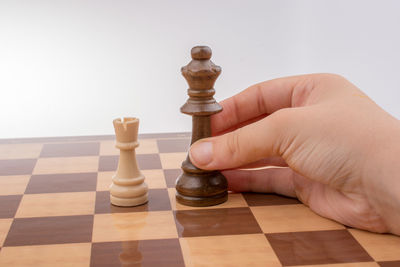 Close-up of hand holding wooden king piece on chess board over white background