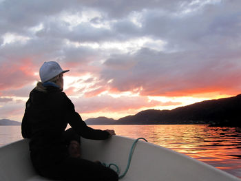 Man sitting on boat in sea against sky during sunset