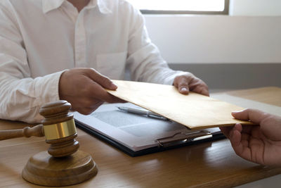 Midsection of lawyer with client holding envelope over office desk