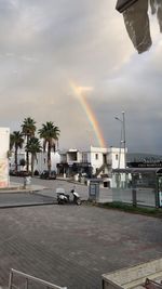 Rainbow over road by building against sky