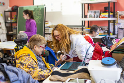 Smiling female nurse with disabled woman using laptop at nursing home