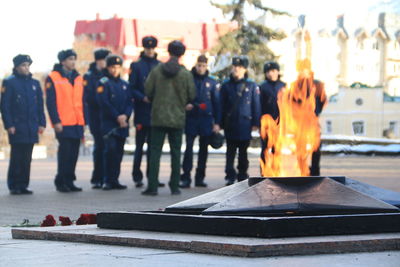 Fire burning at memorial with people standing in background