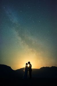 Silhouette bride and groom standing on field against sky at night