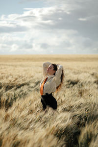 Side view of young mindful female in formal wear with tie and closed eyes among spikes in countryside