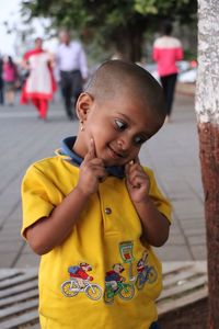 Close-up of boy with fingers on cheeks standing on road