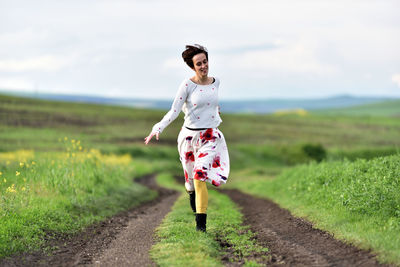 Full length of woman running on walkway amidst grassy field against sky