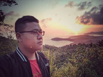 Portrait of young man standing on land against sky during sunset