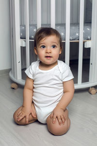 Child in white clothing one year sitting on the floor next to his round white bed