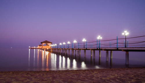 Illuminated bridge over sea against sky at dusk