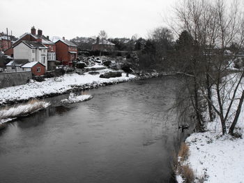 Frozen river amidst buildings and trees against sky