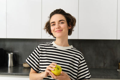 Portrait of young woman holding apple on table at home