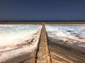 Scenic view of sea against clear sky and path across pink salt mine