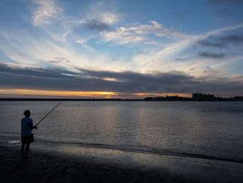 Rear view of man on beach against sky during sunset