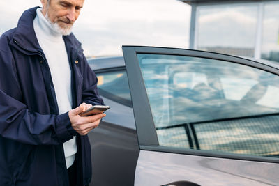 Man using mobile phone while standing by car