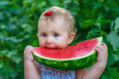 Cute girl eating watermelon against plants