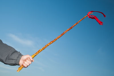 Cropped hand of person holding equipment against blue sky