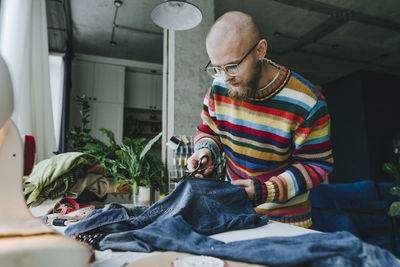 Fashion designer cutting denim fabric on table in workshop