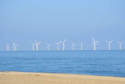 Wind turbines on beach against clear blue sky
