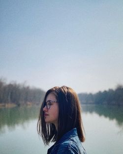 Close-up of woman looking away against lake against clear sky