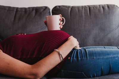 Midsection of pregnant woman with cup lying on sofa