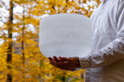 Midsection of woman holding autumn leaf against trees