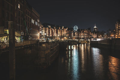 Illuminated buildings by river against sky at night