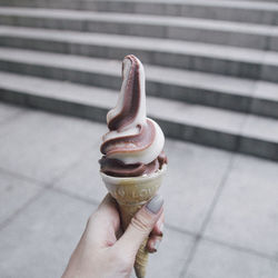 Cropped hand holding ice cream cone against steps