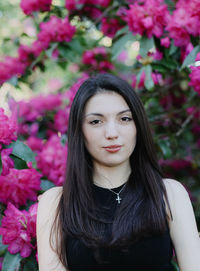 Portrait of one beautiful girl with long hair  stands near a flowering bush of pink rhododendron