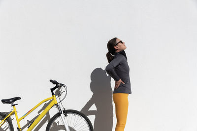 Woman cyclist with lower back pain standing by the bike holding and massaging her back.
