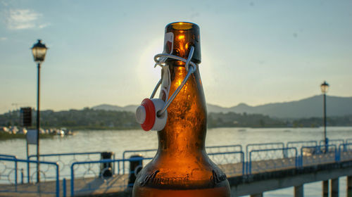 Close-up of beer bottle by railing against lake