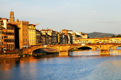 Arch bridges over arno river by buildings against sky