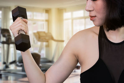 Midsection of woman lifting dumbbell in gym