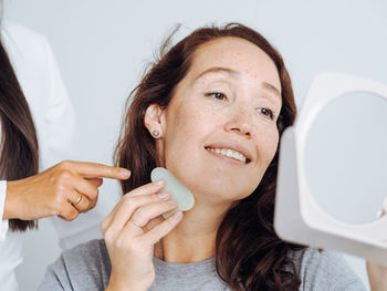 Middle age woman and cosmetologist making massage anti age procedures with guasha stone