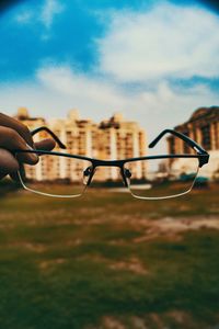 Cropped hand holding eyeglasses against sky