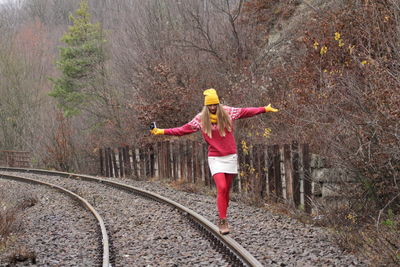 Woman balancing on railroad track against bare trees during winter
