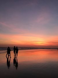 Silhouette people on beach against sky during sunset