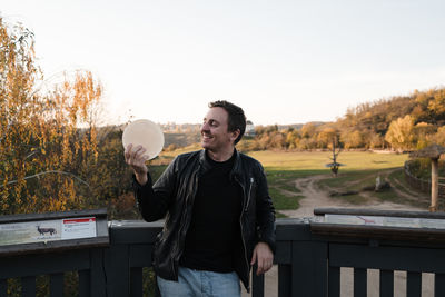 Man looking away while standing by railing against sky