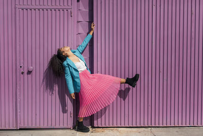 Side view of woman standing against pink wall